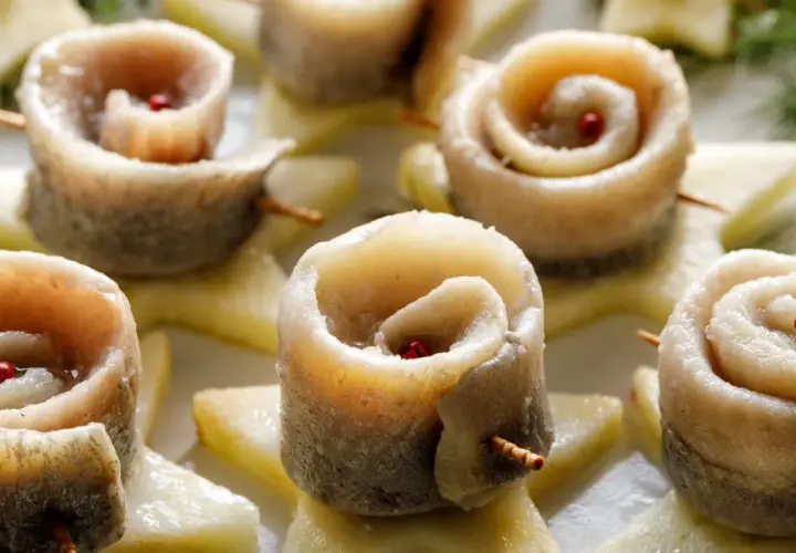 Roladki ze śledzi w occie, ozdobione ziarnami pieprzu, ułożone na plasterkach jabłka.