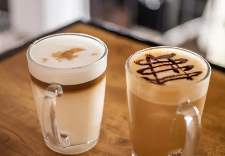 Dwie pyszne kawy latte, jedna z czekoladowym wzorem, druga z pianką i cynamonem. Idealne na chwilę relaksu.