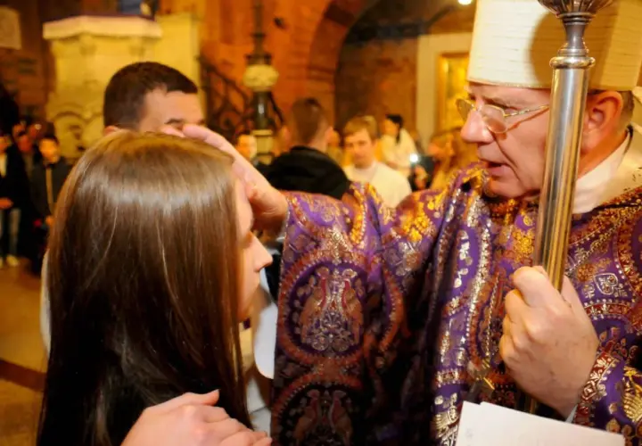 Biskup w bogato zdobionej szacie nakłada rękę na głowę dziewczyny, udzielając jej sakramentu bierzmowania. To ważny krok, jak załatwić bierzmowanie.