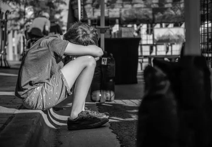 Chłopiec skulony na chodniku, zamyślony. Leczenie psychiatryczne a opieka nad dzieckiem to trudne wyzwania dla rodziny.