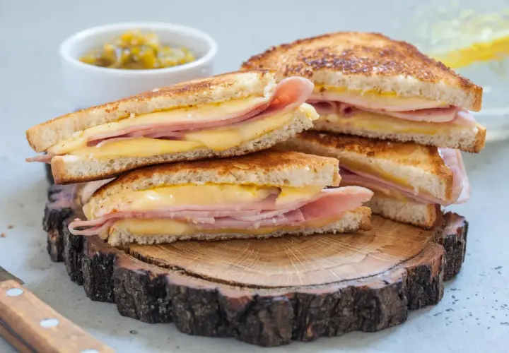 Pile de croque monsieur dorés, garniture généreuse de jambon et fromage fondant, servis sur une tranche de bois rustique.