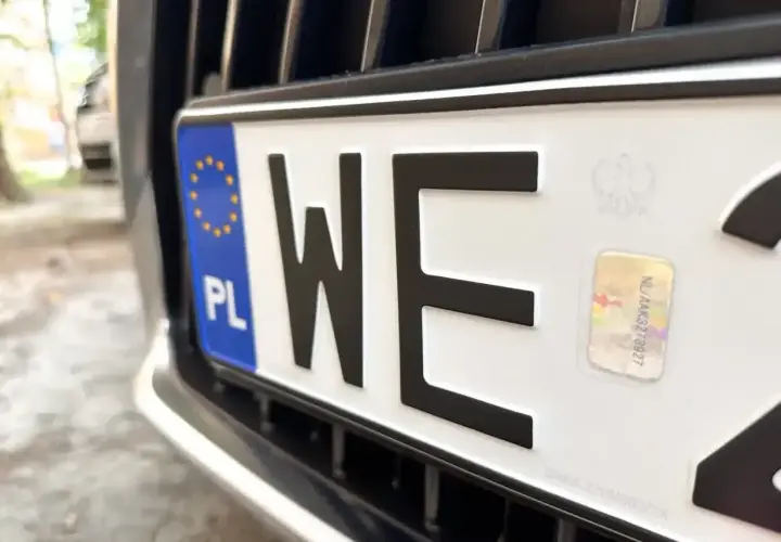 Zbliżenie na polską tablicę rejestracyjną z literami "WE". Widoczny symbol Unii Europejskiej i hologram.