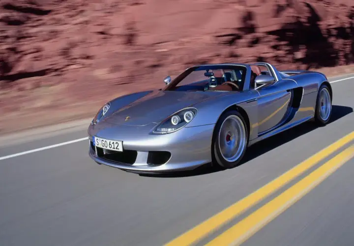 Srebrny Porsche Carrera GT pędzi po pustynnej drodze, zostawiając za sobą rozmyte czerwone skały.