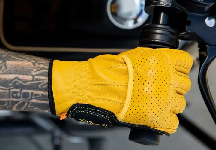 Mano tatuata con guanti Biltwell gialli traforati, pronti per un giro in moto.
