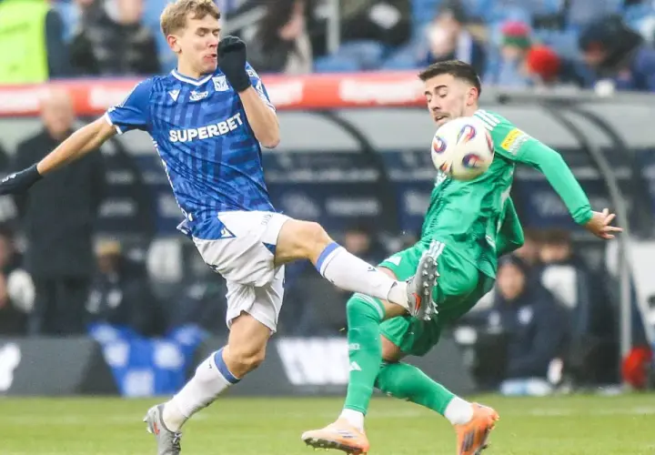 Dwóch piłkarzy walczy o piłkę. Jeden w niebieskiej koszulce, wychowanek Lecha Poznań, próbuje odebrać futbolówkę przeciwnikowi w zielonym stroju.