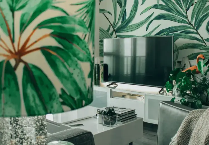 Sala de estar con papel tapiz de hojas tropicales. Muebles DM blancos y un televisor moderno.