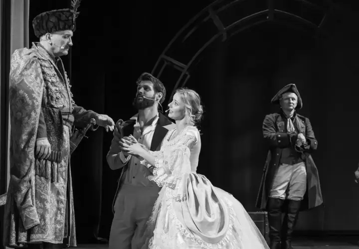 Aktorzy w historycznych strojach na scenie. W centrum młoda para, obok nich starszy mężczyzna w bogatym stroju. To piękny **teatr u przyjaciół**.