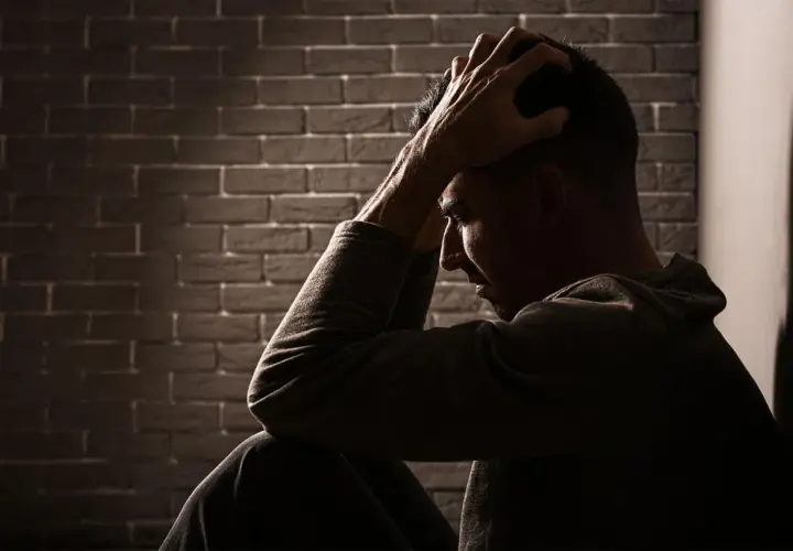 Uomo seduto con le mani tra i capelli, illuminato da un raggio di luce. Potrebbe cercare sollievo con stabilizzatori dell'umore naturali.