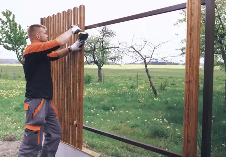 Pracownik dokonuje montażu sztachet drewnianych, przykręcając je do metalowej konstrukcji.