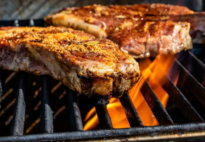 Deux entrecôtes au grill, assaisonnées et grillées à la perfection, avec des flammes vives en dessous.