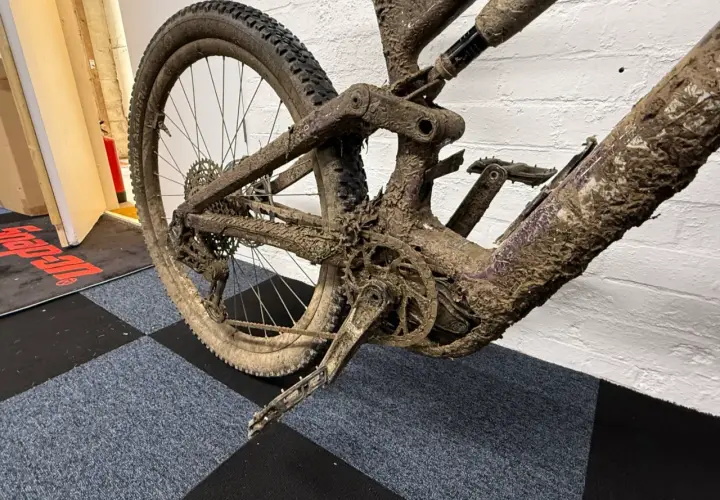 Mud-caked mountain bike rear triangle and wheel. This looks like it will be an expensive bike service cost.