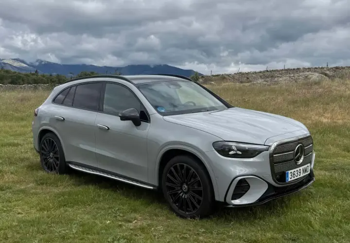 Un SUV gris moderno, con tracción 4 matic, descansa en un campo verde con montañas nubladas al fondo.