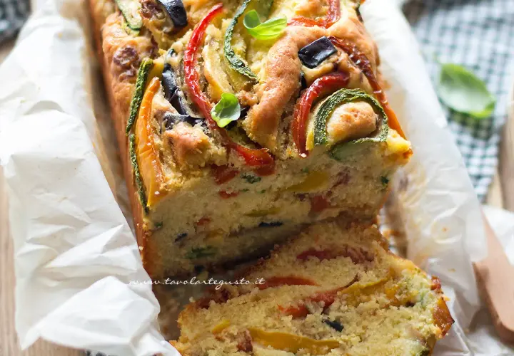 Plumcake salato ricco di verdure colorate come zucchine, peperoni e olive, guarnito con basilico fresco.