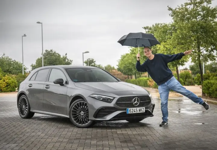 Hombre con paraguas posa junto a un Mercedes Clase A gris. ¡Una prueba de conducción bajo la lluvia!