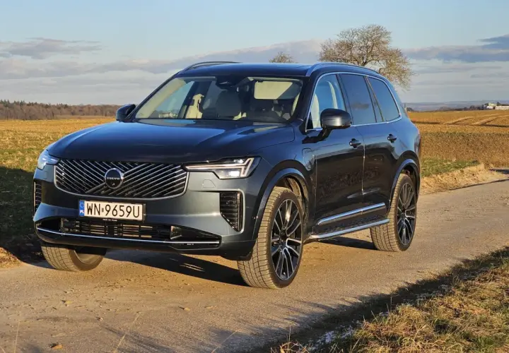 Ciemnoszary Volvo XC90 T8 na drodze polnej, z polami i drzewami w tle.