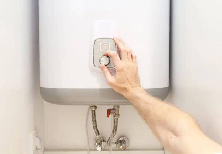 Mano ajustando el control de temperatura de un termo eléctrico.