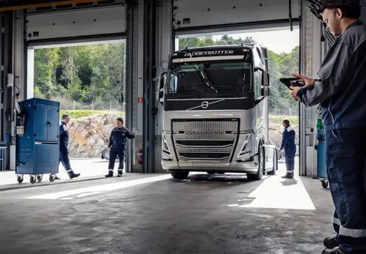 Mechanicy w serwisie obsługują nowoczesną ciężarówkę Volvo FH4. Jeden z nich sprawdza coś na tablecie.