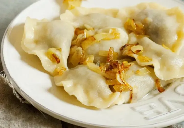 Pyszne pierogi ruskie na talerzu, polane skwarkami z cebulki. Idealne, gdy wiesz, jak długo gotować pierogi ruskie.