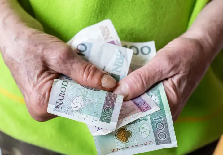 Dłonie trzymają polskie banknoty: 10, 20 i 100 zł. Ile pieniędzy na start w grze Monopoly?