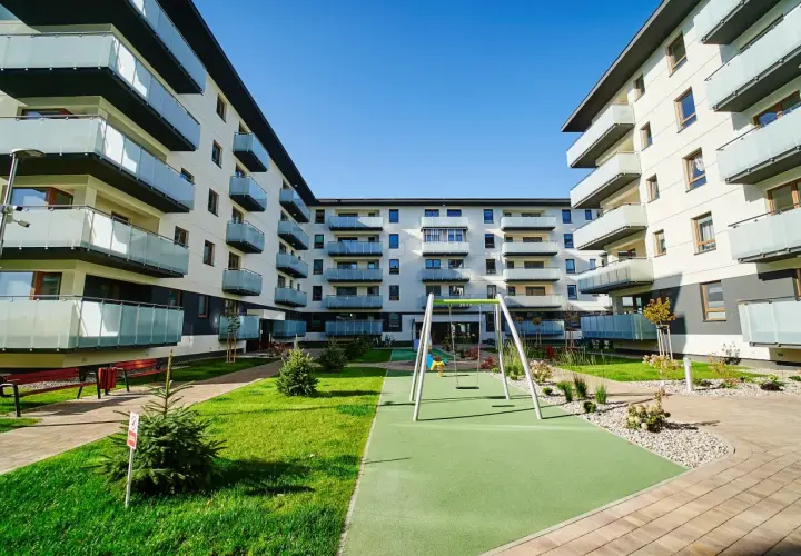 Nowoczesny **piano park** z placem zabaw i zielenią między budynkami mieszkalnymi.