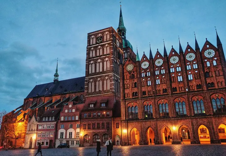 Abendstimmung im **Stralsund Zentrum**: imposante Backsteingotik mit Kirchturm und Rathaus, beleuchteter Marktplatz mit wenigen Passanten.
