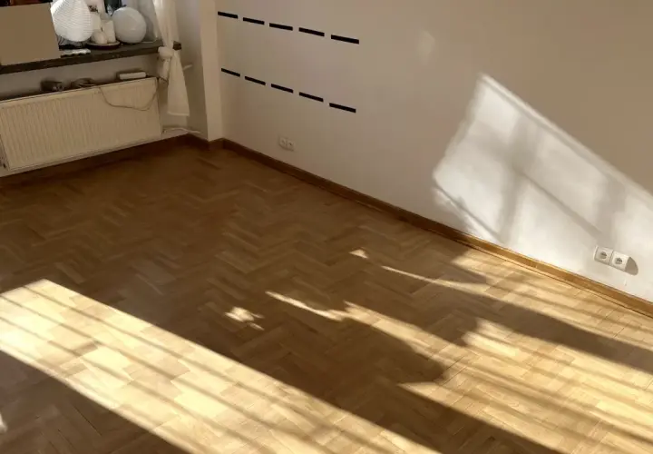Jasne, drewniany parkiet w jodełkę i białe ściany. Brak listew przypodłogowych, co daje nowoczesny wygląd.