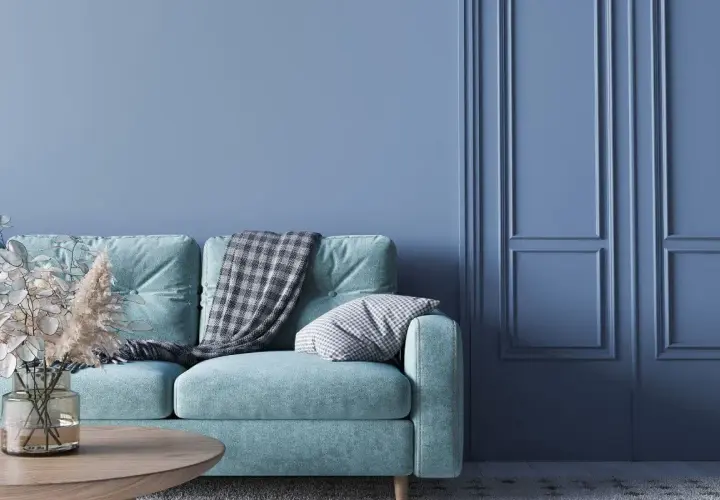 Miętowa kanapa z kocem i poduszką na tle ścian w kolorze baby blue. To znaczy spokój i świeżość.