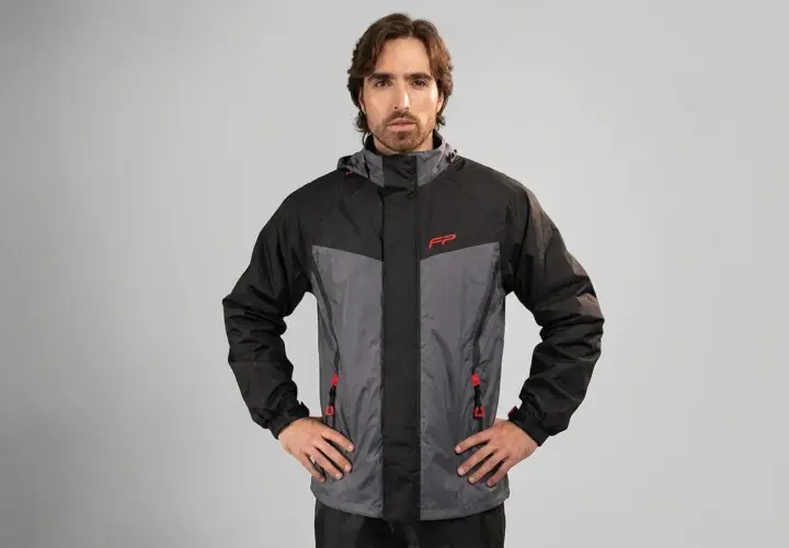 Hombre posando con una prenda impermeable que protege de la lluvia, chaqueta de dos tonos gris y negro con detalles rojos.