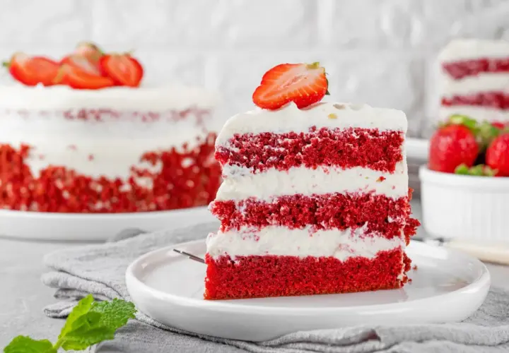 Kawałek tortu red velvet z kremem i truskawkami na talerzu.