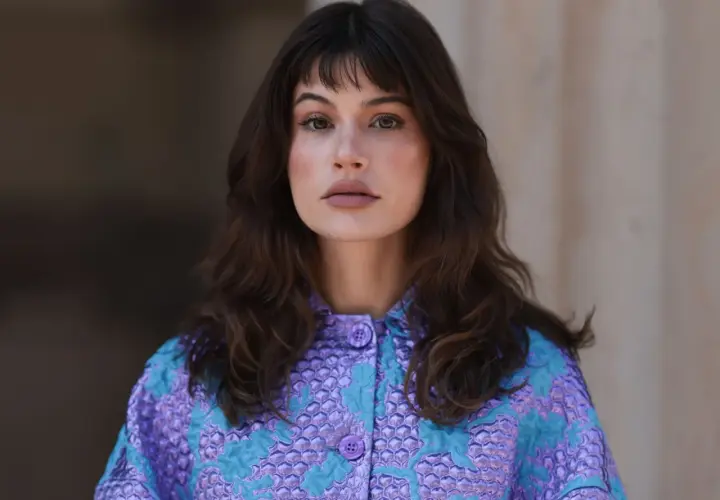 Mujer con melenas cortas con volumen, flequillo y un llamativo abrigo morado y turquesa.