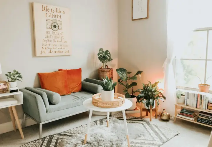 Gemütliches kleines Wohnzimmer skandinavisch einrichten mit grauem Sofa, orangefarbenen Kissen, Pflanzen und einem inspirierenden Bild.
