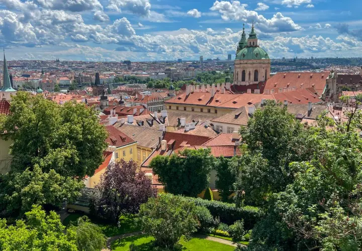Widok na dachy Pragi z zielonym ogrodem. W oddali widać kopułę kościoła. Idealne miejsce, by zobaczyć w Pradze piękno architektury.