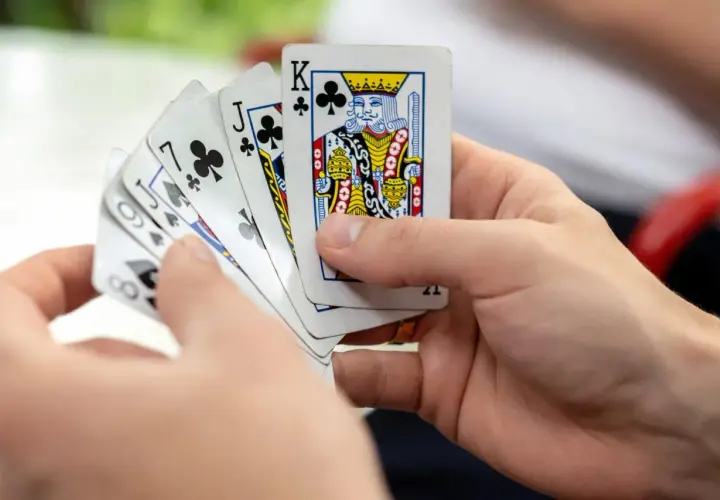 Ręce trzymają karty do gry, wśród nich Król trefl. Czy to początek emocjonującej gry w kuku?