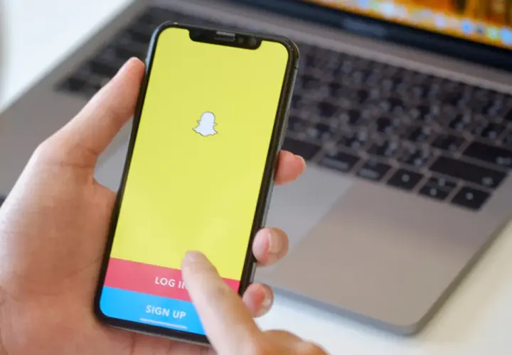 Dłoń trzyma smartfon z logo Snapchata. Widoczny ekran logowania, który może pomóc w procesie jak usunąć konto na snapie.