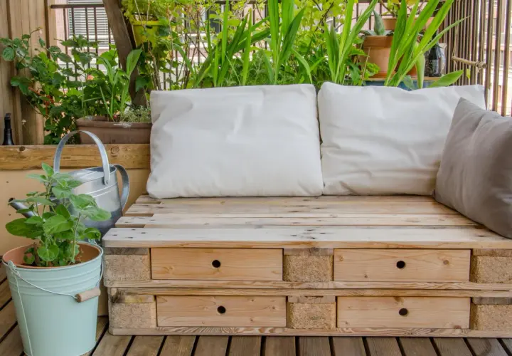 Bequeme Sitzbank aus Paletten mit Schubladen, umgeben von grünen Pflanzen. Tolle Ideen aus Paletten für Balkon und Garten.