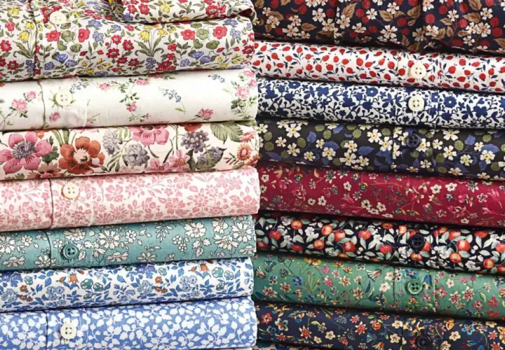 Stacks of folded shirts showcase vibrant, small floral prints, a hallmark of what is liberty fabric.