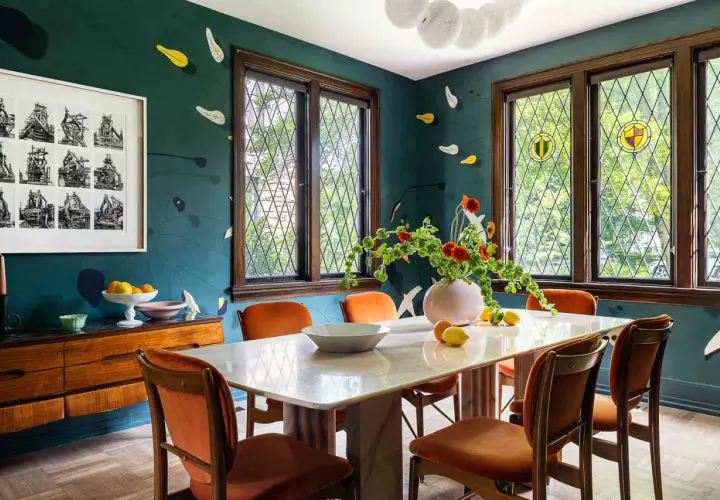 A vibrant kitchen and dining room design featuring a marble table, orange chairs, and a dark teal wall with playful accents.