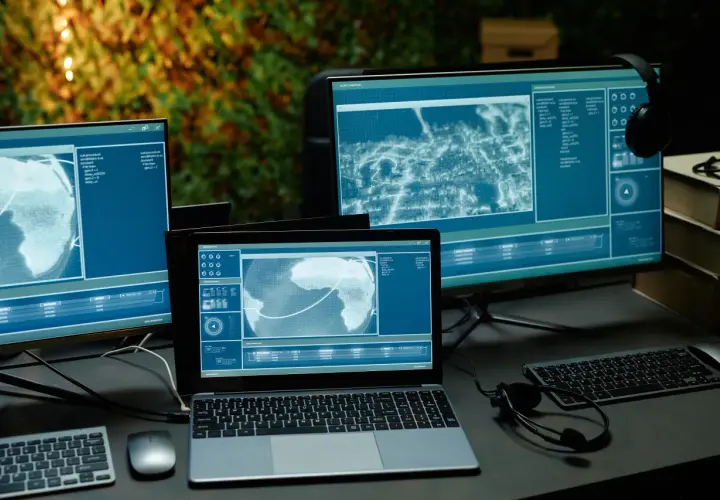 Kilka monitorów i laptop wyświetlających dane i mapy w niebieskich barwach.