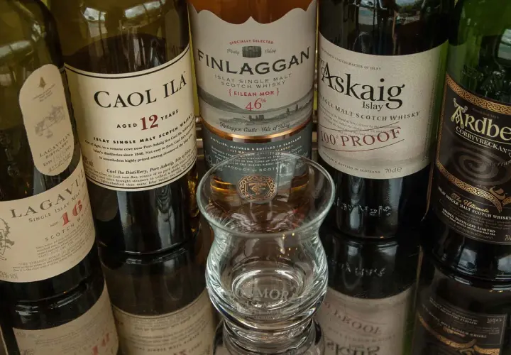 Bouteilles de whisky Islay tourbé : Caol Ila, Lagavulin, Finlaggan, Port Askaig, Ardbeg. Un verre à dégustation vide est au centre.