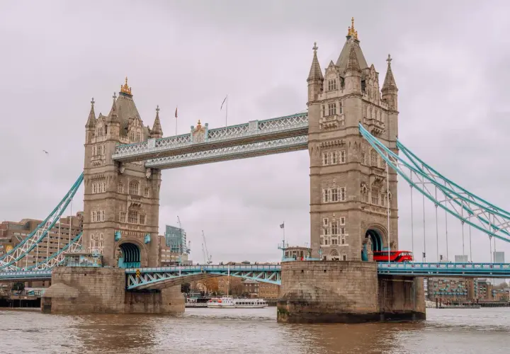 Tower Bridge w Londynie, symbol miasta, opowiada swoją historię. Czerwony autobus przejeżdża przez most, a w tle widać nowoczesne budynki.