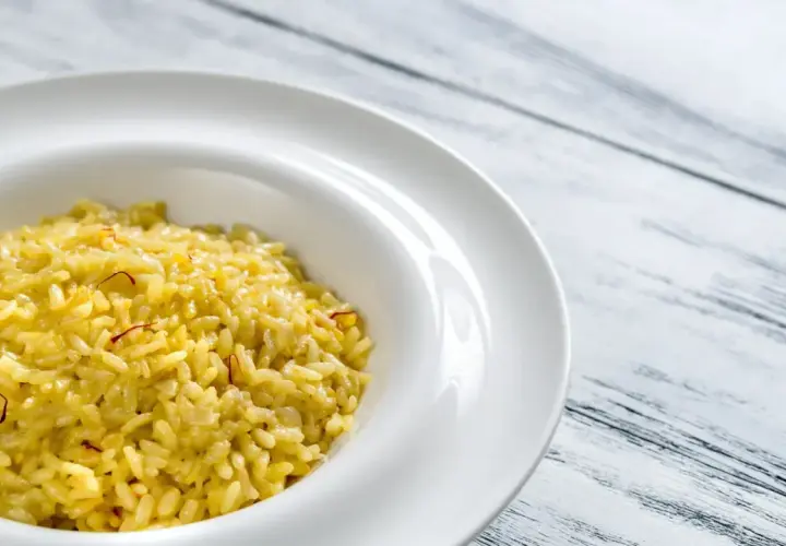 Un crémeux risotto alla milanese, orné de fils de safran, dans une assiette blanche sur fond de bois clair.