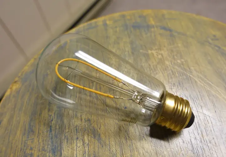 Bombilla de filamento regulable, con un diseño vintage y un filamento amarillo en forma de bucle, descansa sobre una superficie de madera desgastada.