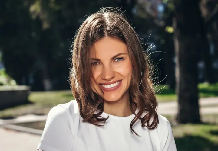 Uśmiechnięta brunetka w białej koszulce, idealna do zadawania pytań do nowo poznanej osoby.