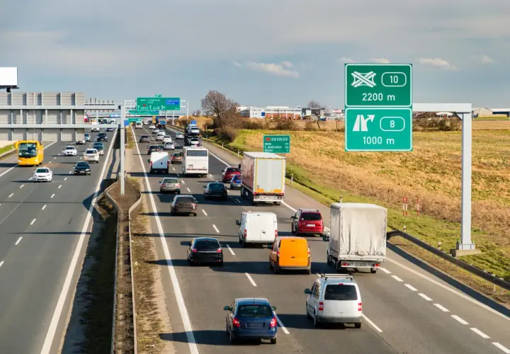 Ruch na autostradzie w Czechach, z samochodami i ciężarówkami pędzącymi z dużą prędkością. Znaki drogowe wskazują kierunki i odległości.