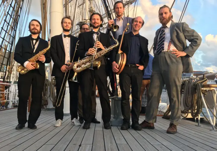 Ett storbandsjazz-band i Stockholm, med musiker som spelar saxofon, trumpet och banjo, poserar på ett fartyg.