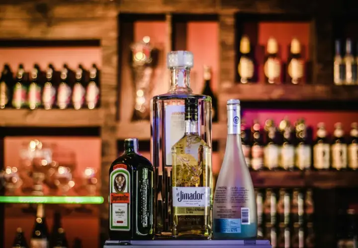 Butelki alkoholu: Jägermeister, El Jimador, Absolut i Hypnotiq na tle półek z napojami.