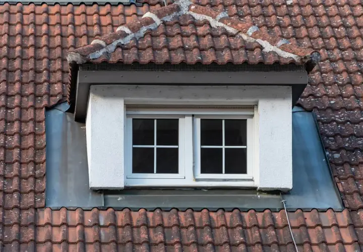 Dachgaube mit zwei Fenstern, umgeben von roten Dachziegeln. Die Bleiverkleidung zeigt, wie man eine dachgaube richtig abdichten kann.