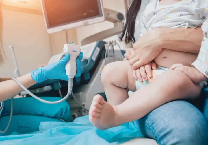 Lekarz wykonuje usg przezciemiączkowe u niemowlaka. Dziecko siedzi na kolanach rodzica, a lekarz trzyma sondę aparatu USG.