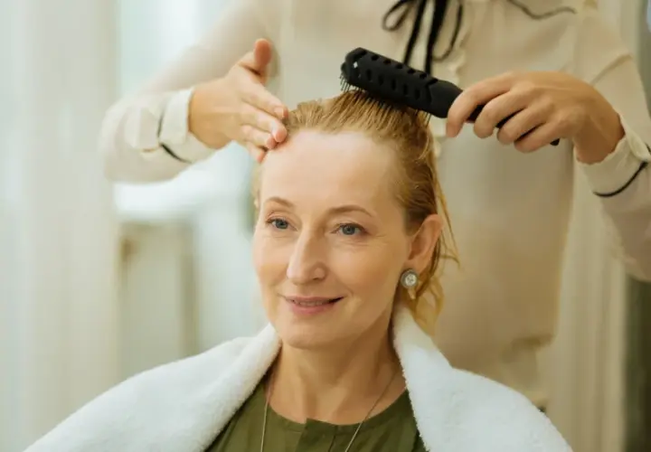 Stylist czesze blondynce cienkie i rzadkie włosy, przygotowując ją do nowej fryzury.