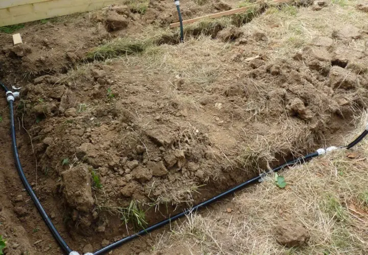 Des tranchées creusées révèlent des tuyaux noirs, prémices de réseaux enterrés pour l'irrigation ou le drainage.